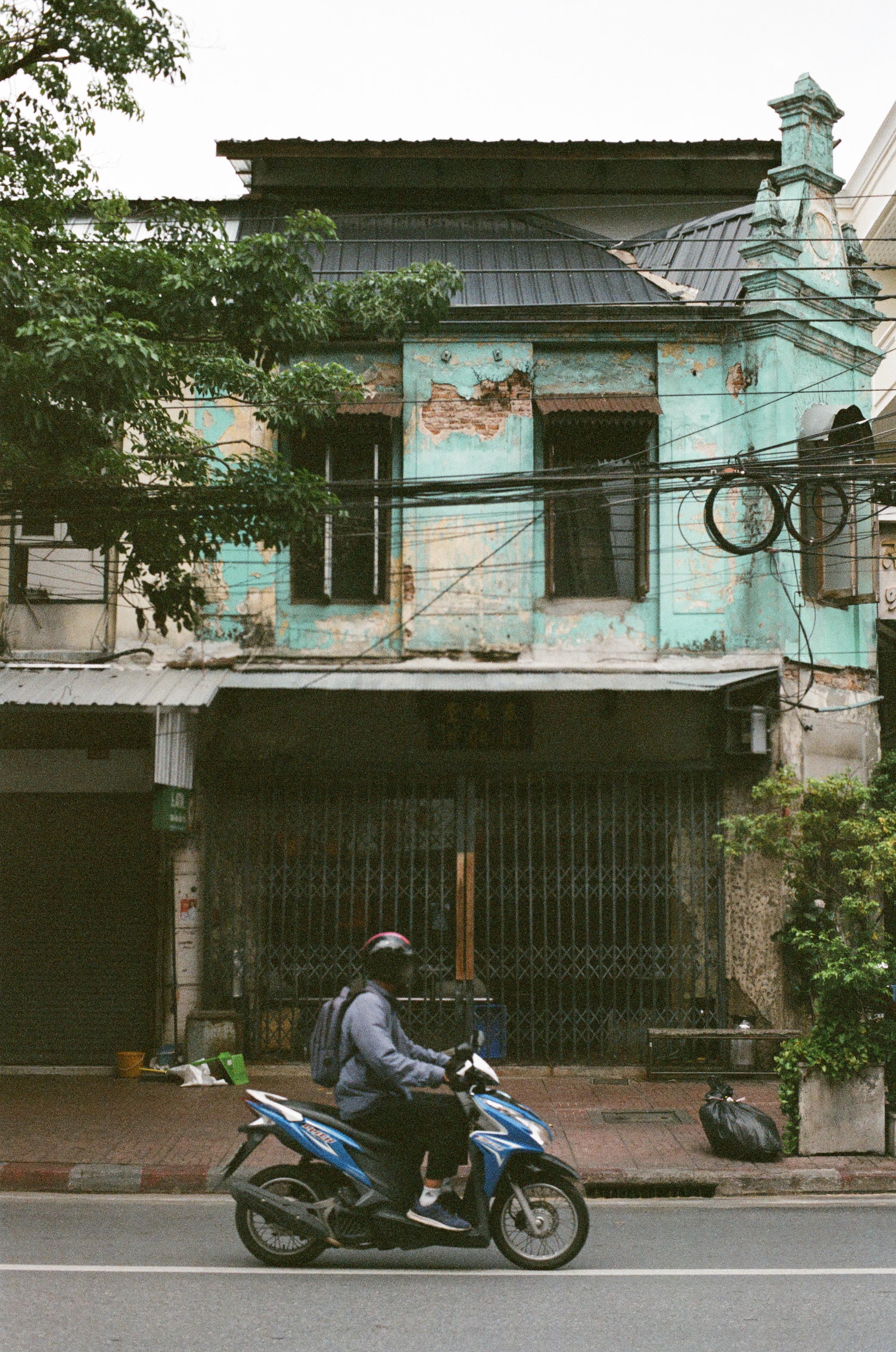 A man riding a scooter from left to right in Bangkok's Chinatown.