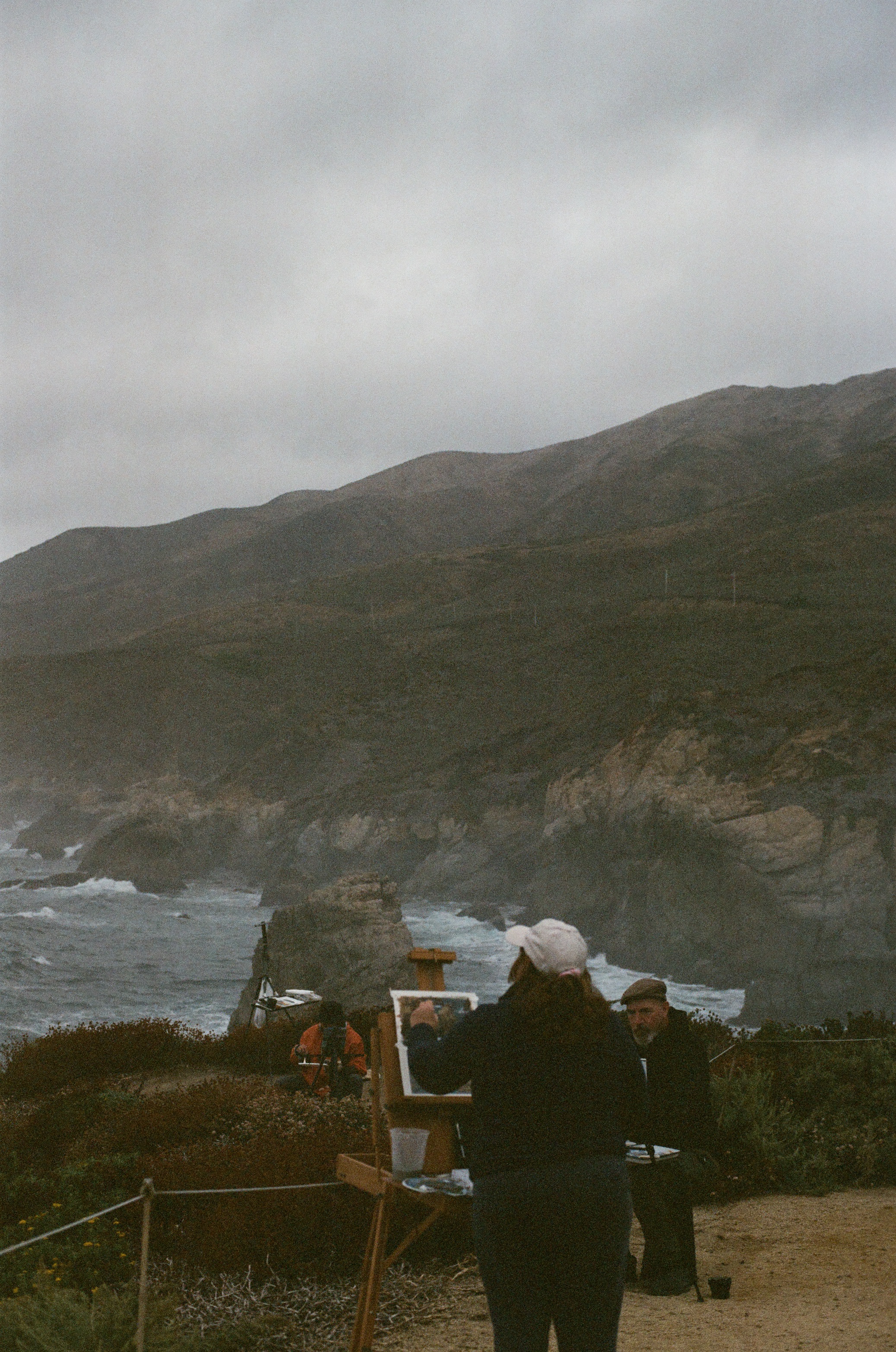 A photo of a woman looking out into the ocean while painting a picture of the scenery.